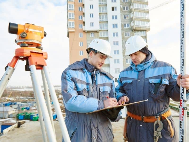 Surveyors using leveling equipment on a high-rise construction site to check vertical alignment, floor layout, and structural positioning accuracy.